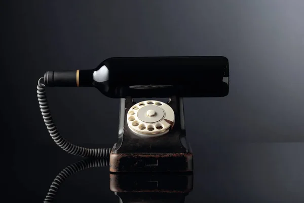 Old black phone and bottle of red wine on a black reflective bac — Stock Photo, Image