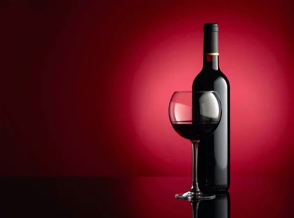 Glass and bottle of red wine on a dark red background. Copy spac — Stock Photo, Image