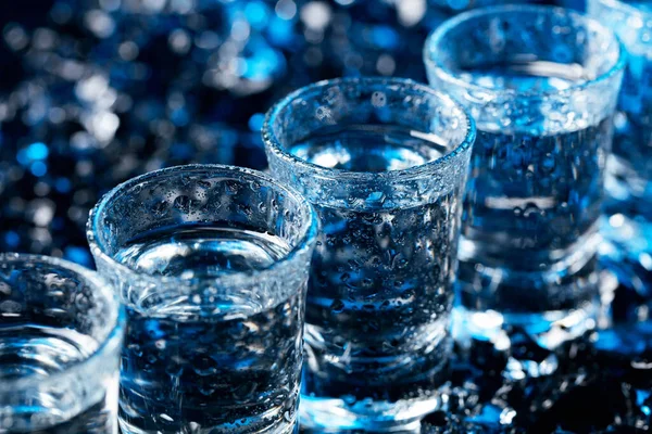 Damp glasses of vodka with ice on a black reflective background. — Stock Photo, Image