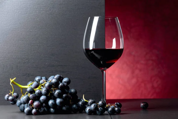 Blauwe druiven en glas rode wijn op een zwarte tafel. — Stockfoto