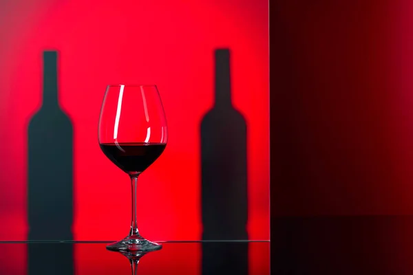 Botellas y copa de vino tinto sobre fondo rojo . — Foto de Stock