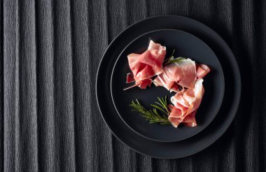 Prosciutto and rosemary on a black plate. Top view.