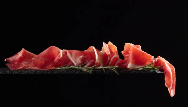 Prosciutto med rosmarin på svart bakgrund. — Stockfoto