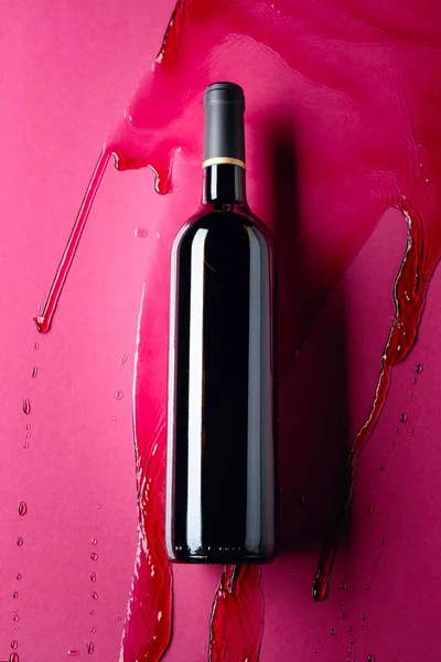 Closed bottle of red wine and splashes on a red background. — Stock Photo, Image