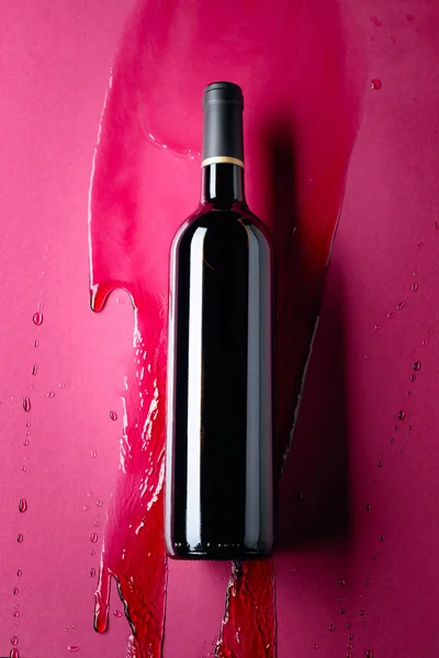 Closed bottle of red wine and splashes on a red background. — Stock Photo, Image