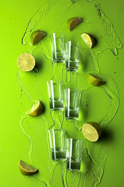 Small shot glasses with lime slices and flowing tequila on a gre — Stock Photo, Image