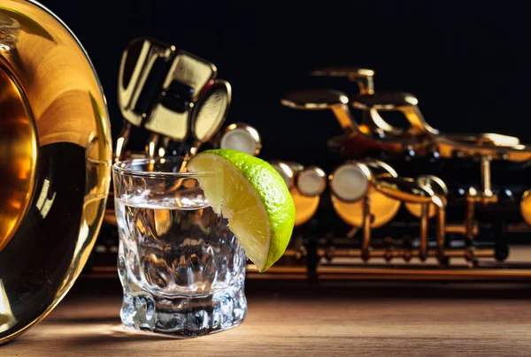 Saxofon och tequila med lime på ett träbord. — Stockfoto