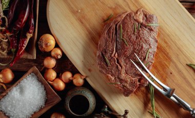 Baharatlı pişirilmemiş biftek eski ahşap bir masada biberiye.