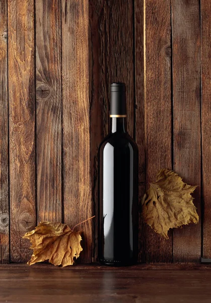 Eski ahşap arka planda bir şişe kırmızı şarap ve kurutulmuş asma yaprağı. İçeriğiniz için boş alan.