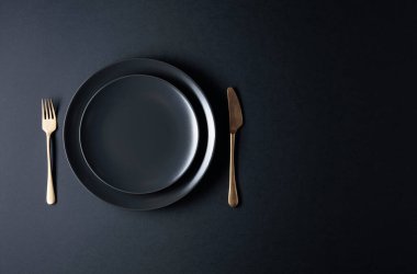Siyah arka planda boş bir siyah plaka, çatal ve bıçak. Üst görünüm, alanı kopyala.
