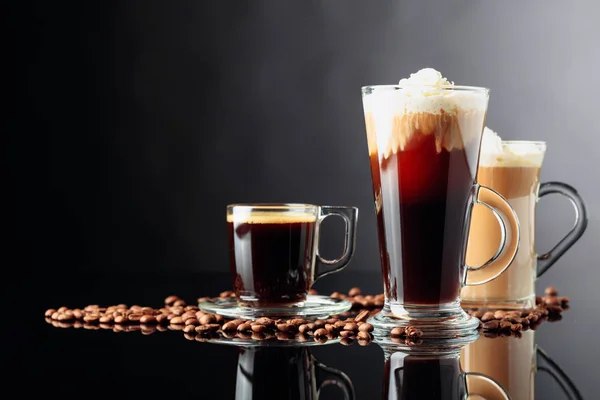 Coffee drinks and coffee beans on black reflective background. Espresso, latte and Irish coffee.