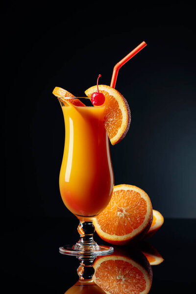 Tequila Sunrise cocktail with orange and cherry on a black reflective background.