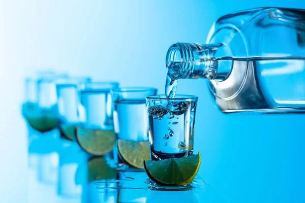 Tequila Plastrami Limonki Niebieskim Tle Nalanie Mocnego Napoju Alkoholowego Małych — Zdjęcie stockowe