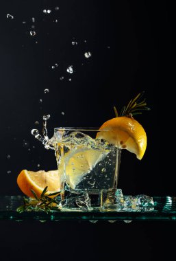 Limonlu ve biberiyeli cin tonik. Cam sehpada buz parçaları olan karbonatlı bir içecek. Siyah arkaplan, boşluğu kopyala.