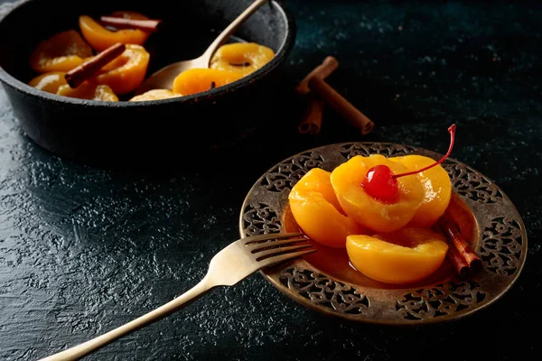 Peach dessert with cinnamon and  cherry on a dark background.