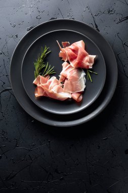 Siyah tabakta Prosciutto ve biberiye. Üst görünüm, alanı kopyala.