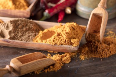 Zerdeçal, köri ve zencefil tozu. Eski ahşap bir masada ahşap kaşıklarla çeşitli Doğu baharatları..