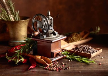 Çeşitli biber ve baharatlı klasik biber değirmeni. Ahşap bir masa üzerinde mutfak aletleri, baharatlar ve biberiye ile eski biber değirmeni. 