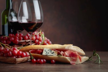 Jambon, mavi peynir ve karanlık bir arka plan üzerinde biberiye ile sandviç. Lezzetli aperatif ve bardak kırmızı şarap. Metniniz için kopya alanı.