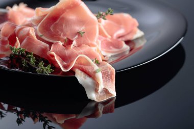 Siyah tabakta kekik olan bir Prosciutto. Siyah yansıtıcı arkaplan.