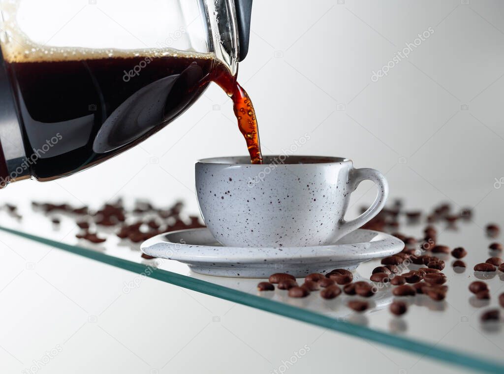 Black coffee in a ceramic cup on a glass table. Coffee is poured from the coffee maker into a cup. Copy space.