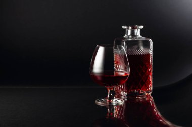 Bir bardak brendi ve koyu arkaplanda bir sürahi. Siyah refleksli arka planda süslü bir yansıma. Boşluğu kopyala.