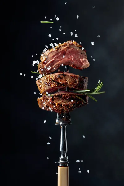 烤牛肉牛排 背景是黑色的香料 牛肉牛排 叉子上撒满迷迭香和海盐 — 图库照片