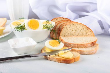 Beyaz ahşap bir masada haşlanmış yumurta ve ekmek..