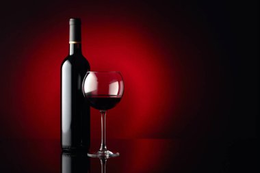 Siyah yansıtıcı arka planda cam ve bir şişe kırmızı şarap. İçeriğiniz için boş alan.
