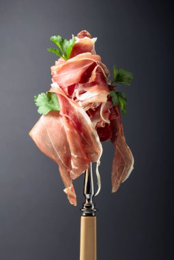 Çatalla maydanozlu ince dilimlenmiş jambon. Geleneksel İtalyan mutfağı. Siyah arkaplan.