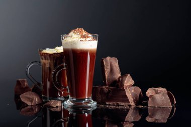 Krem şantili sıcak çikolata ve koyu arkaplanda siyah çikolata parçaları. Boşluğu kopyala.