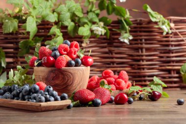 Eski bir ahşap masanın üzerinde çilek, yaban mersini, ahududu ve tatlı kiraz çilek çekim renkli çeşitli karışımı. Yaprakları ile çeşitli sulu çilek.