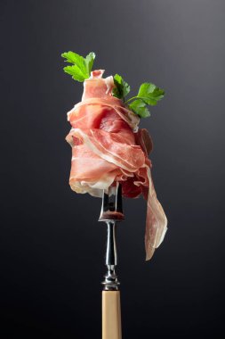 Çatalla maydanozlu ince dilimlenmiş jambon. Geleneksel İtalyan mutfağı. Siyah arkaplan.