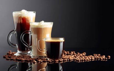 Espresso, latte macchiato ve kahve çekirdekli siyah yansıtıcı arka planda İrlanda kahvesi. Boşluğu kopyala.
