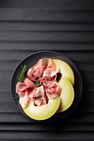 Prosciutto Met Rozemarijn Meloen Een Zwarte Plaat Bovenaanzicht Kopieer Ruimte — Stockfoto