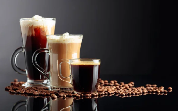Espresso, latte macchiato and Irish coffee on black reflective background with coffee beans. Copy space.