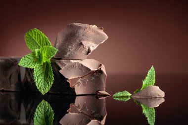 Siyah yansıtıcı arka planda naneli büyük bir parça koyu acı çikolata. Boşluğu kopyala.