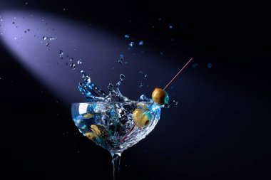 Yeşil zeytinli martini. Bardakta kokteyl ve su sıçraması. Metnin için boşluk kopyala.