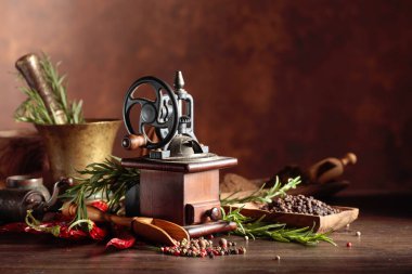 Çeşitli biber ve baharatlı klasik biber değirmeni. Ahşap bir masa üzerinde mutfak aletleri, baharatlar ve biberiye ile eski biber değirmeni. 