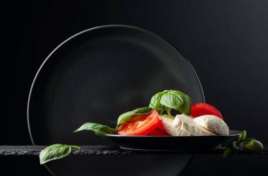 Siyah arka planda domates ve fesleğenli Mozzarella. Boşluğu kopyala.