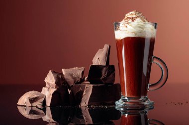 Krem şantili sıcak çikolata ve kahverengi arka planda koyu çikolata parçaları. Boşluğu kopyala.