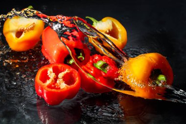 Kırmızı ve sarı kırmızı kırmızı kırmızı biber siyah bir zemine sıçrıyor.