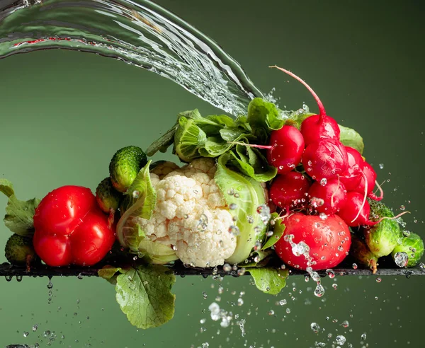 Various raw vegetables with water splash. Cauliflower, tomato, cucumber, radish and paprika on a green background.