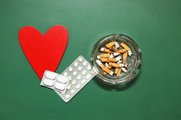 Сердце, таблетки и окурки на зеленой деревянной поверхности. По — стоковое фото
