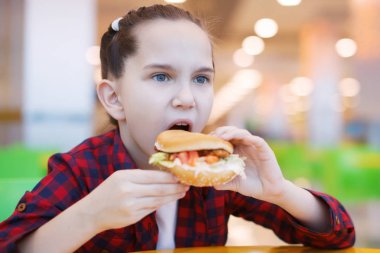 Sevimli gülümseyen küçük kız bir hamburger yiyor