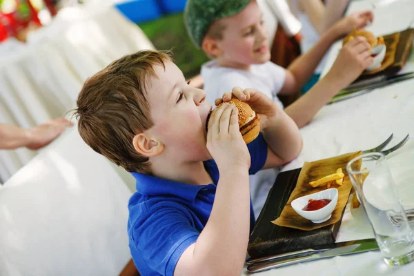 Μικρό αγόρι τρώει χάμπουργκερ σε ένα καφέ, έννοια των τροφίμων — Φωτογραφία Αρχείου