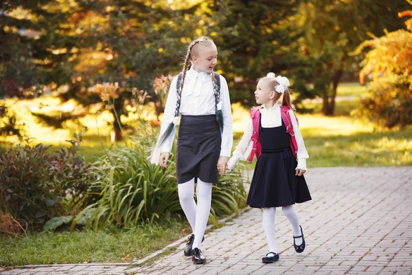 Duas meninas Schoolgirls ir na estrada no outono Parque e falar uns com os outros — Fotografia de Stock