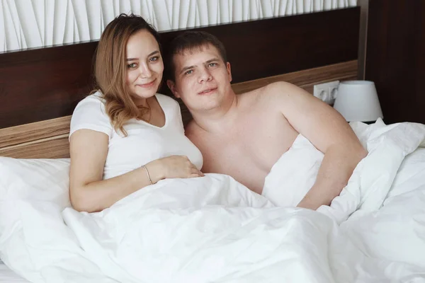 Giovane bel marito e moglie a riposo a letto sotto una coperta bianca in una camera d'albergo — Foto Stock