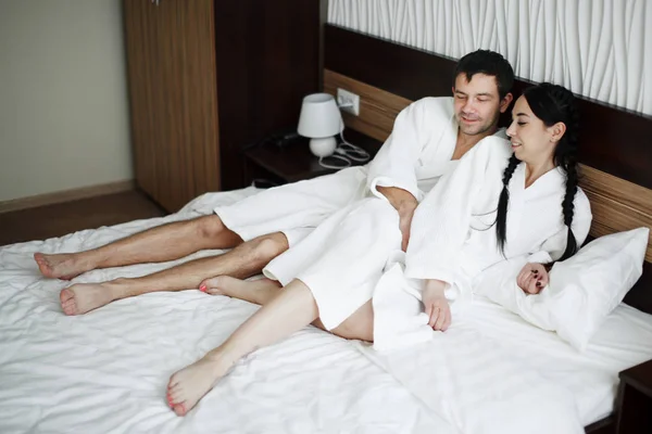 Молодой муж и жена белых халатов играть и улыбаться в постели в — стоковое фото