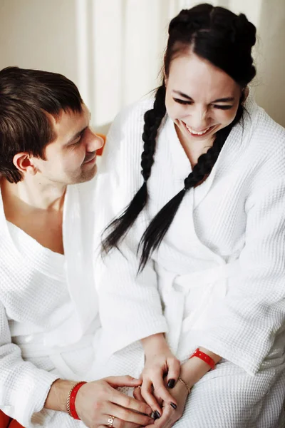 Joven esposo y esposa de batas blancas juegan y sonríen en un sillón naranja en una habitación de hotel. De cerca. . — Foto de Stock